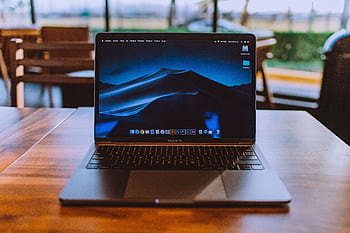 A sleek laptop on a wooden table in a cozy indoor setting, perfect for remote work. HD wallpaper