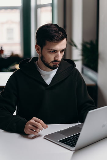 A focused young man using a laptop at a desk in a stylish home office setting. HD phone wallpaper