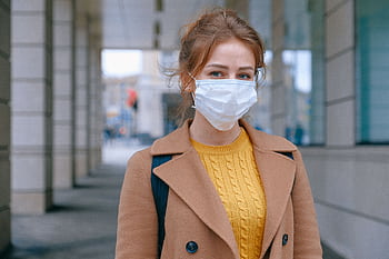 Young woman in a coat and mask stands outdoors, promoting health and safety measures. HD wallpaper