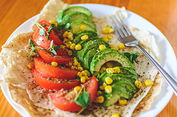 A vibrant salad with avocado, tomato, and corn on flatbread, topped with herbs, perfect for a healthy meal. HD wallpaper