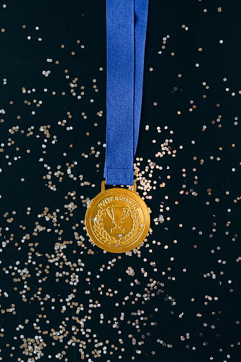 Close-up of a shimmering gold medal with blue ribbon on a black surface, symbolizing victory and achievement. HD phone wallpaper