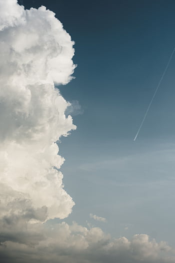 Majestic cloud formation against a deep blue sky with a visible aircraft contrail. HD phone wallpaper