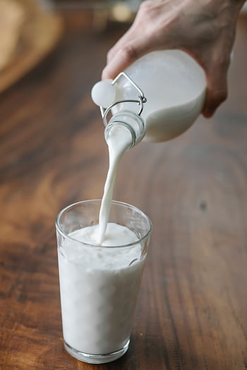 A glass being filled with fresh organic milk indoors on a wooden table. HD phone wallpaper