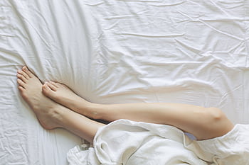 Peaceful morning scene with woman's legs resting in bed under white sheets. HD wallpaper