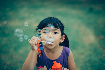 Adorable young girl enjoying summer outdoors while blowing bubbles, capturing pure childhood joy. HD wallpaper