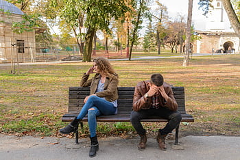 An upset couple seated on a park bench, expressing frustration during an autumn day. HD wallpaper