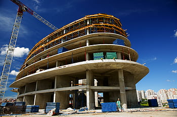 Low angle view of a circular building under construction with a crane, clear blue sky. HD wallpaper