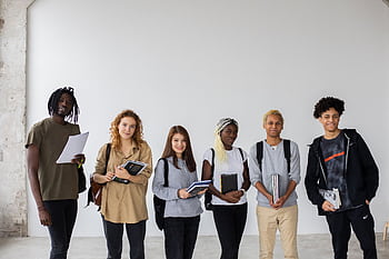A diverse group of six young adults smiling indoors, holding textbooks, symbolizing unity and teamwork. HD wallpaper