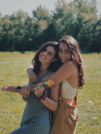 Two smiling sisters embracing in a sunlit park, enjoying a warm summer day together. HD phone wallpaper