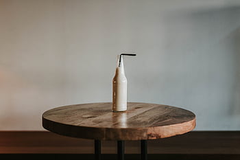 Simple composition of a bottle with straw on a round wooden table, creating a minimalist and modern aesthetic. HD wallpaper