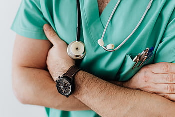 Doctor in scrubs with folded arms and stethoscope, symbolizing confidence in healthcare. HD wallpaper