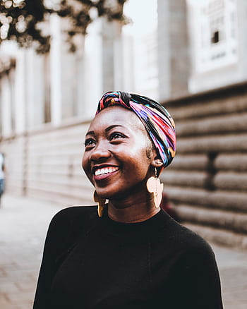 Smiling woman wearing vibrant headscarf and earrings, captured in an urban street setting. HD phone wallpaper