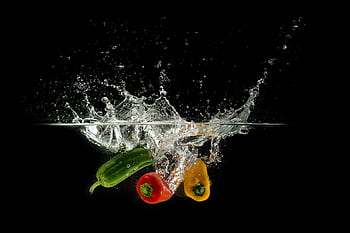 Colorful bell peppers splashing in clear water against a dark background. HD wallpaper