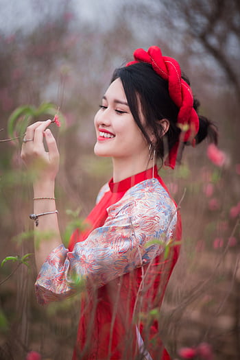 Smiling young woman in traditional dress enjoying flowers in a spring field. HD phone wallpaper