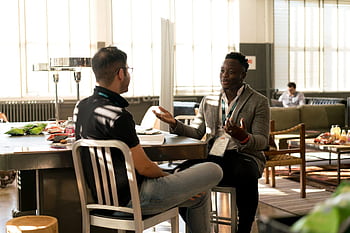 Two men having a casual discussion in a bright indoor setting, highlighting mentorship. HD wallpaper