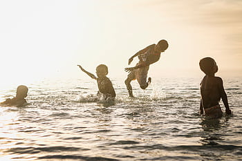 Young kids having fun splashing in the sea with sunlit background. HD wallpaper