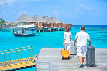 A couple arriving at a luxurious Maldives resort dock with luggage, capturing a tropical vacation vibe. HD wallpaper