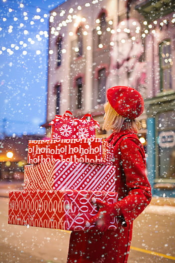 Woman carrying red holiday gifts in snowy city street, embracing winter festivities. HD phone wallpaper