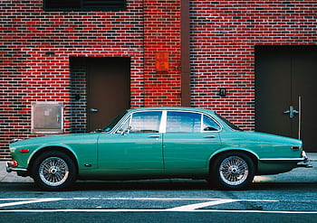 Vintage green Jaguar car parked in an urban setting against a red brick wall, highlighting classic automotive design. HD wallpaper