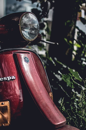 Moody and vintage close-up of a classic red Vespa scooter parked in nature. HD phone wallpaper