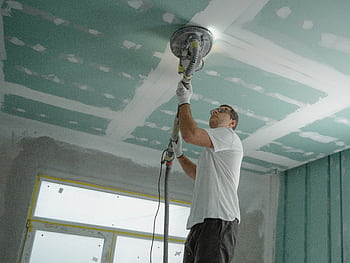 A professional worker sanding the ceiling during a home renovation project. Indoor construction setting. HD wallpaper