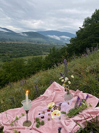 A serene picnic setup on a mountain meadow with flowers and candlelight under a cloudy sky. HD phone wallpaper