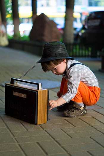 A young boy in fashionable attire adjusts an old-fashioned radio outdoors. HD phone wallpaper