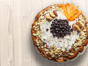 A close-up of a beautifully garnished homemade pie with fruits and nuts on a wooden table. HD wallpaper