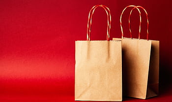Simple brown paper bags with handle on a festive red backdrop, perfect for Christmas. HD wallpaper