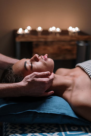 Woman receiving a calming facial massage in a tranquil spa setting with candlelight. HD phone wallpaper