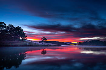 Stunning sunset reflecting over a calm river with colorful sky and silhouetted trees. HD wallpaper