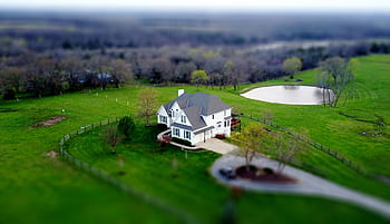 Aerial shot of a charming rural home surrounded by lush green fields and a tranquil pond. HD wallpaper