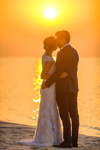 Captivating moment of a couple sharing a kiss during a beach sunset wedding, exuding romance. HD phone wallpaper