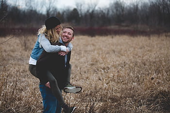 A happy couple enjoys a playful moment in a field during the day, symbolizing love and joy. HD wallpaper