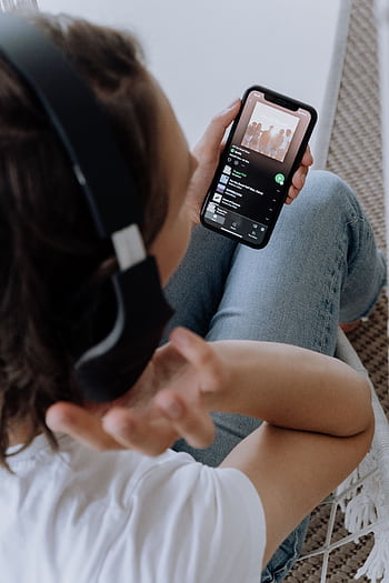 Person wearing heads, using a smart to listen to music in a comfortable setting. HD phone wallpaper