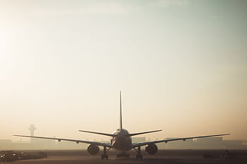 A misty morning scene of a plane on the runway with a hazy sky background, showcasing air travel ambiance. HD wallpaper