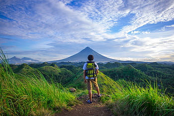 A hiker enjoys the scenic view of Mount Mayon in the lush Bicol countryside. HD wallpaper