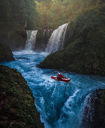 Dramatic scene of a man kayaking down waterfall surrounded by lush forest. HD phone wallpaper