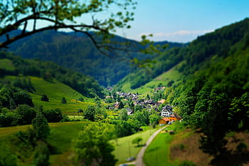 Charming countryside village nestled in a lush, green valley under a bright blue sky. HD wallpaper