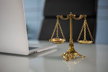 Golden justice scales on a desk beside a laptop, symbolizing law and balance. HD wallpaper