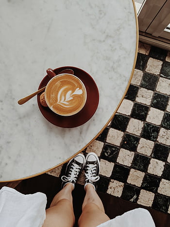 Overhead view of a latte with art on a marble table, sneakers visible on checkered floor. HD phone wallpaper
