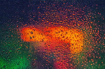 Raindrop-covered glass with vibrant orange and green reflections, creating an abstract effect. HD wallpaper