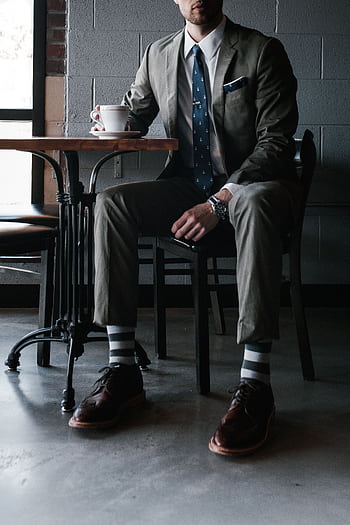 A man in a designer suit enjoys coffee in a chic cafe setting. HD phone wallpaper