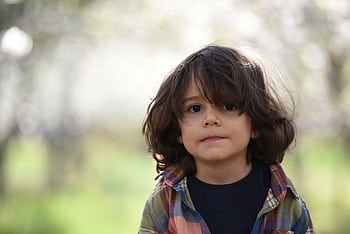 Portrait of a cute child with long hair wearing a plaid shirt, standing outdoors during spring. HD wallpaper