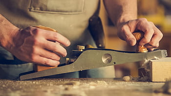 A carpenter skillfully using a hand plane on a wooden surface indoors. HD wallpaper