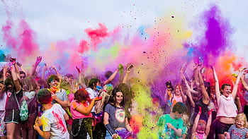 A joyful crowd covered in vivid colors celebrates a festival outdoors with flying powder. HD wallpaper