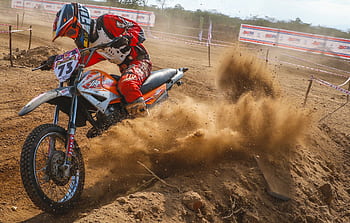Dynamic motocross scene with rider kicking up dust on a dirt track. HD wallpaper