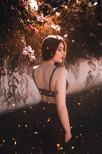 A young woman posing outdoors, bathed in warm sunlight amidst blooming flowers HD phone wallpaper