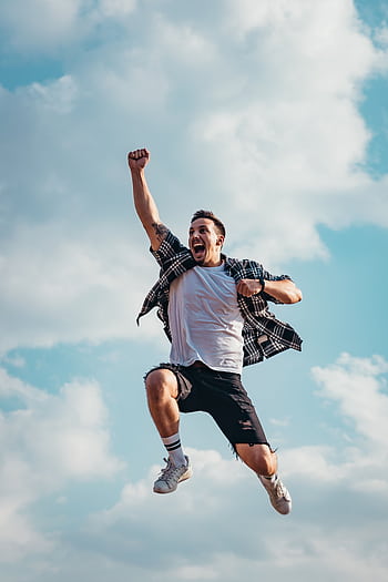 A joyful young man jumps midair with clouds and blue sky in the background, exuding energy and dom. HD phone wallpaper