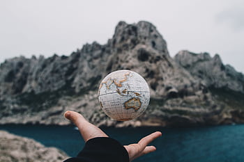 A hand holding a floating globe with a scenic Marseille backdrop, capturing adventure and exploration. HD wallpaper